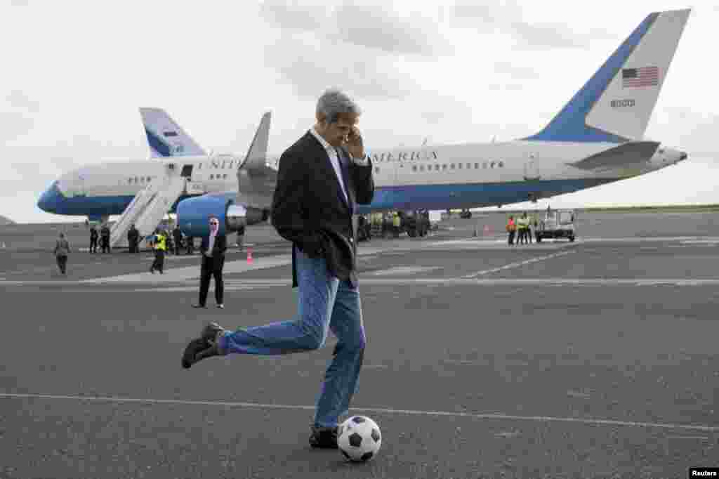 U.S. Secretary of State John Kerry kicks a soccer ball while talking on his cellphone during an airplane refuelling stop en route to Washington on May 5. (Reuters/Saul Loeb)