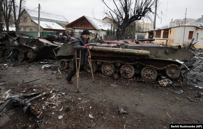 Чоловік на милицях проходить повз знищену українськими військами російську військову техніку у Бучі під Києвом. 1 березня 2022 року