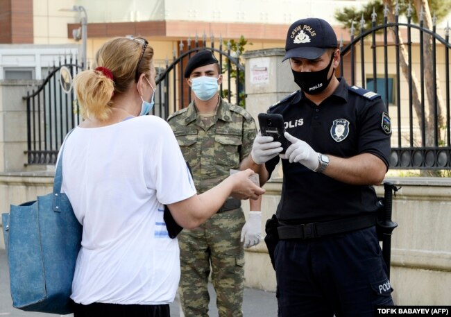 A police officer inspects a woman's documents under the gaze of an Azerbaijani soldier in Baku in July. Azerbaijan deployed troops to help police ensure a tight coronavirus lockdown.