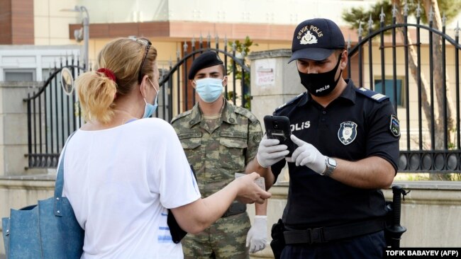 Një oficer policie inspekton dokumentet e një gruaje në Baku, më 3 korrik, 2020.