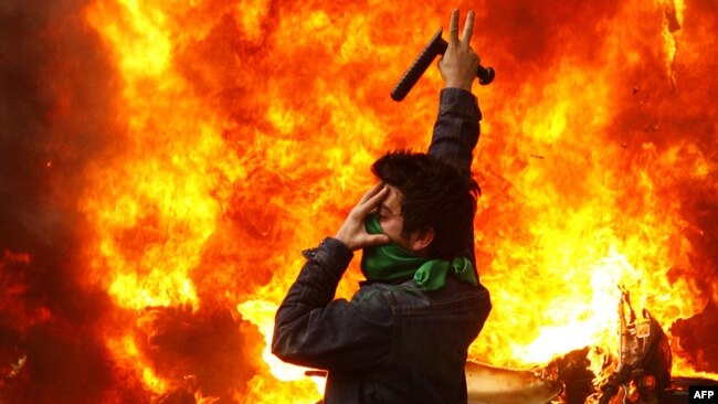 An opposition protester gestures next to a burning police motorcycle set on fire during clashes with security forces in Tehran, 27Dec2009