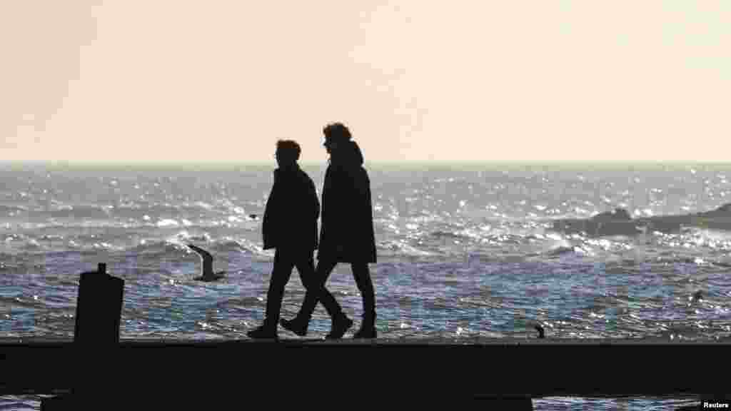Двоє неспішно прогулюються уздовж зимового моря