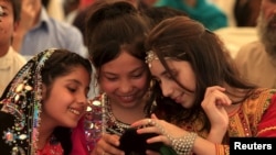 Afghan girls wearing traditional dresses play with a mobile phone. The Taliban says its ban on certain social media applications is aimed to protect younger generations. 