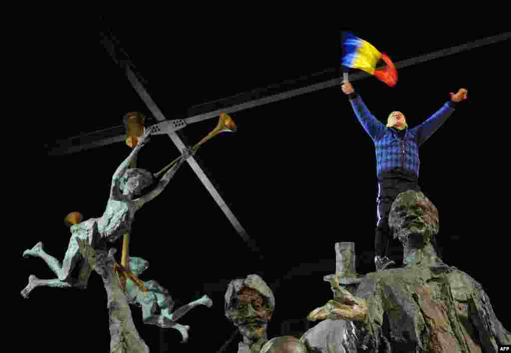 A child shouts antigovernment slogans as he holds a Romanian flag on a statue in Piata Universitatii Square during protests against austerity measures in Bucharest on January 15. (AFP/Daniel Mihailescu)