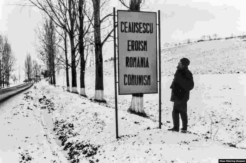 Indicator pe marginea drumului fotografiat în 1988 de un preot olandez în centrul Transilvaniei. Putem citi: &bdquo;Ceaușescu - Eroism, România - Comunism.&rdquo; O astfel de propagandă rutieră era banală în timpul perioadei totalitare. A început prin a se concentra pe obiectivele comunismului. Dar la sfârșitul anilor 1970 și 80, propaganda românească începuse să-i elogieze tot mai mult pe dictatorul Nicolae Ceaușescu și pe soția acestuia, Elena. &nbsp;