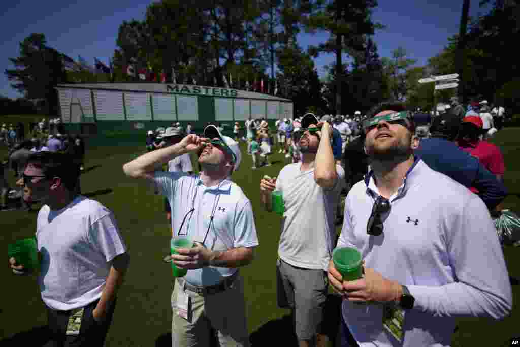 Augusta, Georgia, SUA - Jucătorii de golf se uită la eclipsa de soare în timpul unei runde de antrenament în pregătirea turneului de golf Masters de la Augusta National Golf Club&nbsp;