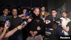 Andrew Tate (centru) și fratele său, Tristan (pardesiu cafeniu), sunt escortați în fața Direcției de Investigare a Infracțiunilor de Criminalitate Organizată și Terorism (DIICOT), în București, 21 august 2024.