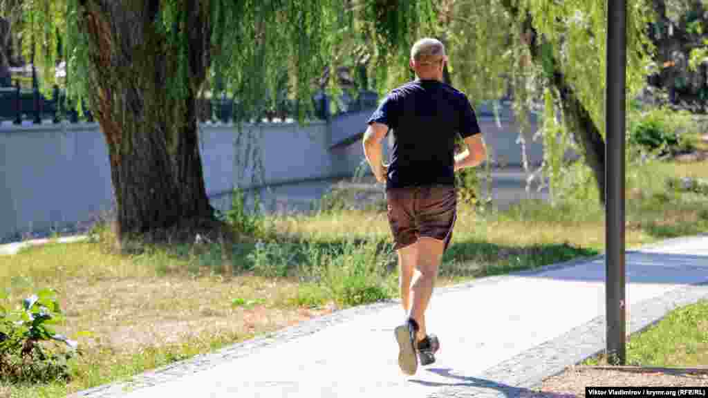 Несмотря на жару, мужчина совершает пробежку по дорожкам парка