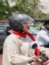 A man and a woman ride their motorcycles past a billboard in the background bearing a portrait of Iran's late president Ebrahim Raisi in central Tehran, on May 21, 2024,