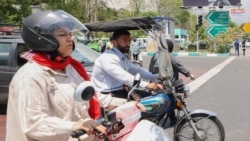 A man and a woman ride their motorcycles past a billboard in the background bearing a portrait of Iran's late president Ebrahim Raisi in central Tehran, on May 21, 2024,