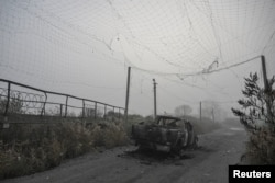 Un vehicul ars, aflat sub o plasă antidrone ruptă, în mijlocul unui drum din apropierea orașului Huliaipole.