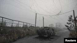 Un vehicul ars, aflat sub o plasă antidrone ruptă, în mijlocul unui drum din apropierea orașului Huliaipole