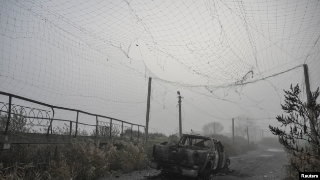 A burned pickup vehicle under a torn anti-drone net in the middle of a road near Hulyaypole.