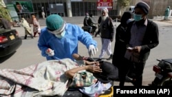 A health-care worker takes a nasal swab from a woman at a COVID-19 testing facility in Karachi. 