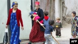 A Tajik girl cleans a rug as two women pass by her in the Tajik capital, Dushanbe. (file photo)