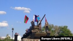 Tineri pozând de Ziua Victoriei pe tancul din centrul Tiraspolului, cu drapele ale Transnistriei, Rusiei și URSS