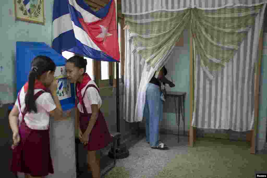 Ten-year-old schoolgirls Claudia Fuentes (right) and Laura Gonzales chat as an elector casts her vote at a polling station in Havana. Municipal elections took place in Cuba on April 19. (Reuters/Alexandre Meneghini)