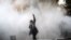 An Iranian woman raises her fist amid the smoke of tear gas at the University of Tehran during a protest driven by anger over economic problems, in the capital Tehran on December 30, 2017.