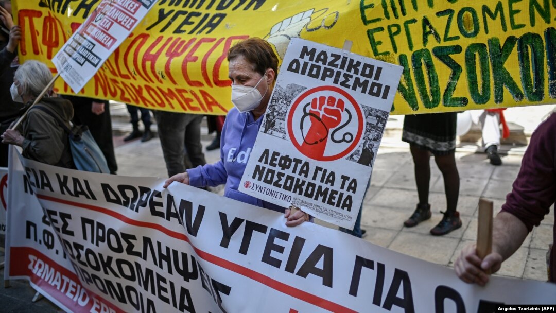 Жена држи плакат „Масовни вработувања, пари за болници“ за време на демонстрациите во Атина, 22.04.2021.