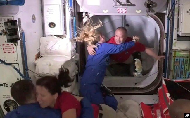 На этом кадре, сделанном по телевидению НАСА, астронавт Соичи Ногучи (на заднем плане справа) приветствует астронавта Кейт Рубинс, когда он входит на Международную космическую станцию из вестибюля между капсулой SpaceX Dragon и МКС ранним вторником, 17 ноября 2020 года.