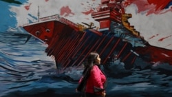 An Iranian woman walking next to a mural on a street in Tehran