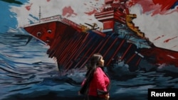 An Iranian woman walking next to a mural on a street in Tehran