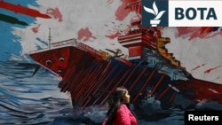Një grua iraniane ec pranë një murali në një rrugë në Teheran.