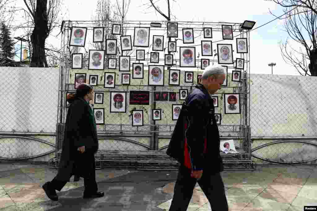 People in Tehran walk in front of pictures of child victims killed in strikes amid the U.S.-Israeli conflict with Iran.