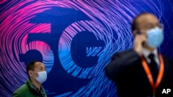 Жаңа технологиялар көрмесіндегі 5G байланыс стандарты жарнамасы ілінген тұстан өтіп бара жатқан маска таққан адамдар. Пекин, Қытай, 14 қазан 2020 жыл.