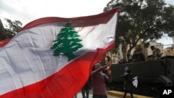 A protester waves a Lebanese flag during a protest against corruption and the failure of long-serving politicians to form a government, in Beirut, Lebanon, Thursday, Nov. 22, 2018. Lebanon is marking 75 years of independence with a military parade Thursda