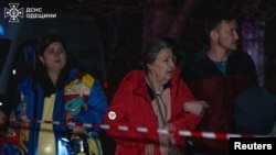 Жители стоят возле своего многоквартирного дома, пострадавшего в результате ночного удара российского беспилотника, 4 декабря 2025 года