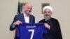 A handout picture released by the office of Iranian President Hassan Rouhani shows him (R) and FIFA President Gianni Infantino holding a football shirt with Rouhani's name during Infantino's visit to the capital Tehran on March 1, 2018.