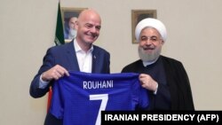 A handout picture released by the office of Iranian President Hassan Rouhani shows him (R) and FIFA President Gianni Infantino holding a football shirt with Rouhani's name during Infantino's visit to the capital Tehran on March 1, 2018.