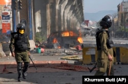 Police officers walk past a burning van set on fire by angry supporters of Tehrik-e Labaik Pakistan during a clash in Rawalpindi in April 2021.