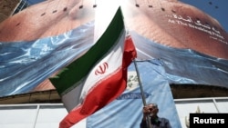 Čovek drži iransku zastavu ispred anti-američkog bilborda u Teheranu, 31. maj 2026. 