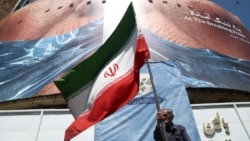 A man in Tehran holds an Iranian flag near an anti-US billboard depicting  US President Donald Trump and the Strait of Hormuz. 