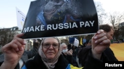 Архивна снимка от демонстрация в Брюксел през март 2025 г., която настоява ЕС да използва замразените руски активи в Европа, за да подкрепи Украйна. Жената на снимката носи плакат с надпис: „Накарайте Русия да си плати“.