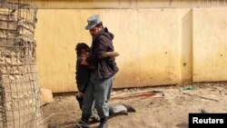An Afghan policeman carrying his wounded comrade after a suicide car bomb attack in Kunduz province on February 10.