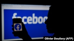Силуэт пользователя со смартфоном на фоне логотипа социальной сети Facebook