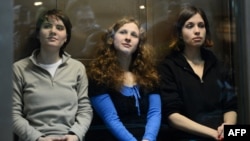 Pussy Riot members Maria Alyokhina (left to right), Yekaterina Samutsevich, and Nadezhda Tolokonnikova sit in a glass-walled cage in a courtroom in Moscow in October 2012 during their trial.