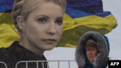 A woman walks in front of a giant poster bearing a picture of jailed Yulia Tymoshenko and a Ukrainian flag on Independence Square in Kyiv 