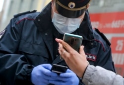 A Russian police officer, wearing a face mask to protect against the coronavirus, checks a woman's "digital permit" to be on the streets of Moscow via a QR code on her smartphone.