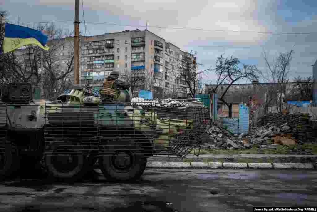 Український бронетранспортер на тлі знищеної будівлі.