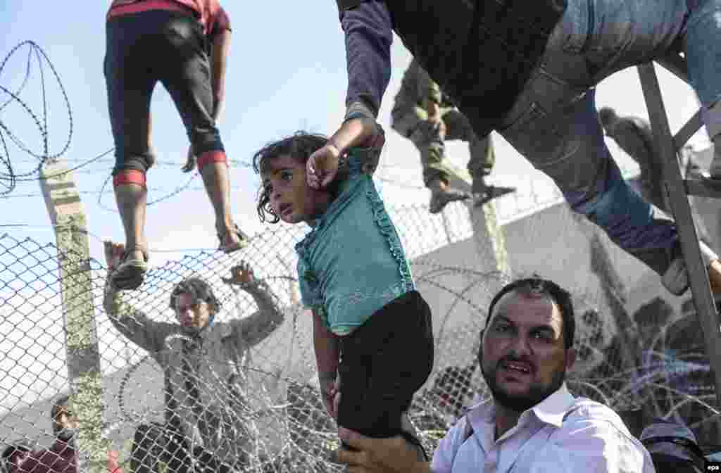 Third Prize stories in the Spot News category was won by Turkish AFP photographer Bulent Kilic.This image from the series shows a Syrian refugee child being lifted into Turkey. (June 14, 2015)