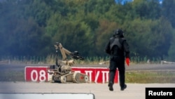 Policajac u zaštitnoj opremi stoji pored robota za deaktiviranje eksploziva na aerodromu Leipzig/Halle u Njemačkoj, nakon što je u augustu u blizini piste pronađen dron.