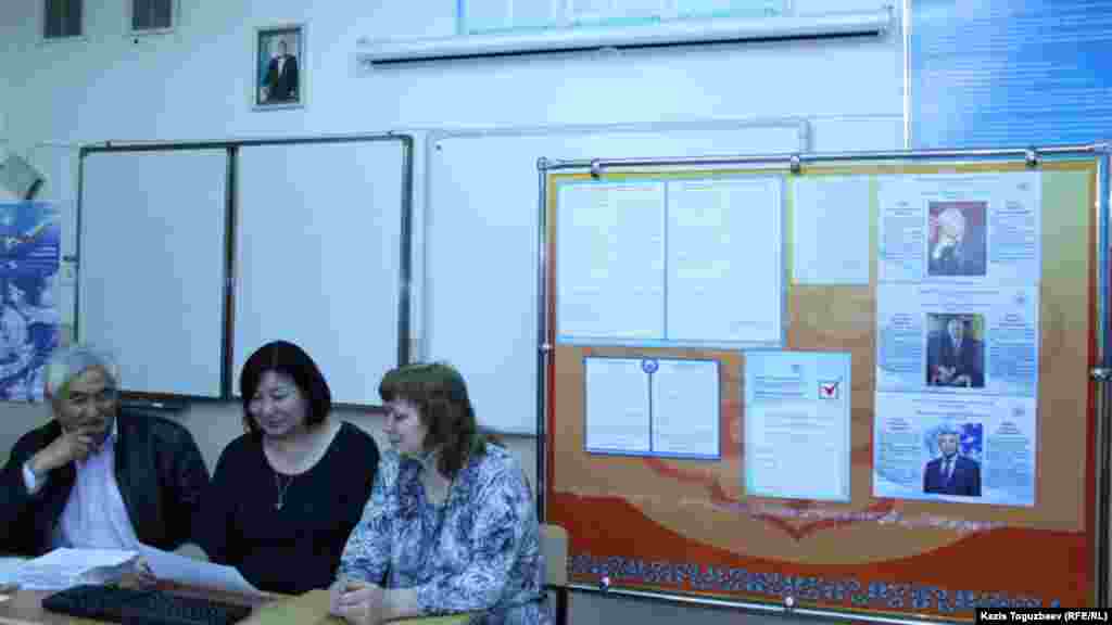 Члены участковой избирательной комиссии в Алматы сидят на фоне агитационных плакатов трех кандидатов и фотографии действующего президента Нурсултана Назарбаева на стене. Алматы, 8 апреля 2015 года.