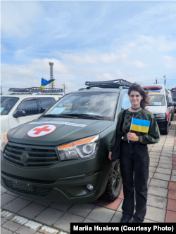 Марія Гусєва стоїть біля автомобілів, які тайванські організації та волонтери передавали для України