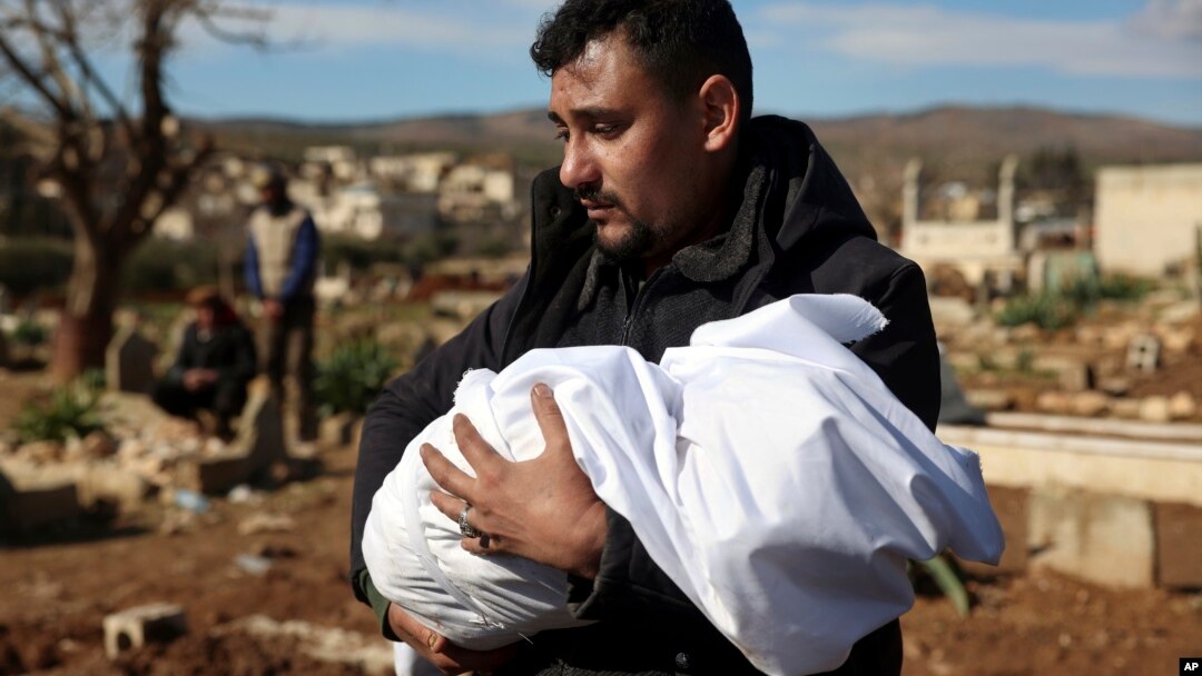 Un bărbat poartă cadavrul unui membru al familiei într-un cimitir din orașul Jinderis, provincia Alep, Siria, marți, 7 februarie 2023