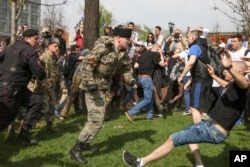 Людина в камуфляжній формі і папасі б'є учасника акції «Він нам не цар» у Москві 5 травня 2018 року