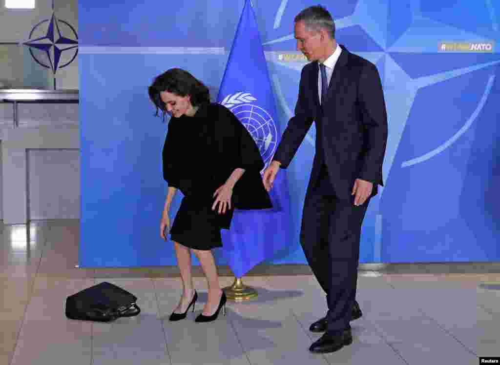 БЕЛГИЈА - Генералниот секретар на НАТО Јенс Столтенберг ѝ помага на актерката Анџелина Џоли да си ја земе чантата за време на заедничката прес-конференција во седиштето на Алијансата во Брисел. Џоли, која е специјален претставник на ОН за бегалци, рече дека користењето силување како оружје за војување не смее да биде прифатливо и побара од НАТО да преземе водство во одвраќањето од злосторства врз жените во конфликтните подрачја.